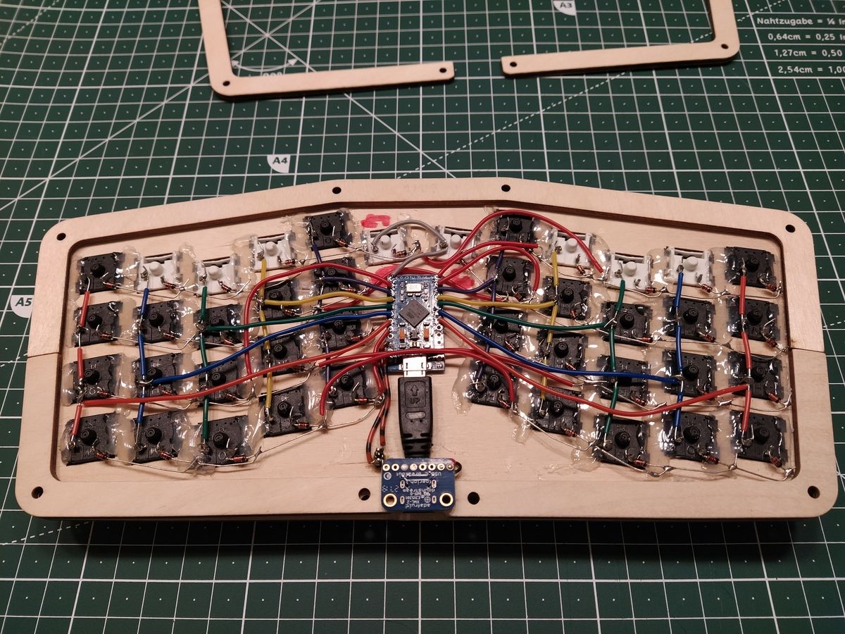 Bottom view of keyboard upside-down showing USB-C breakout board and green Pro Micro controller mounted inside wooden case