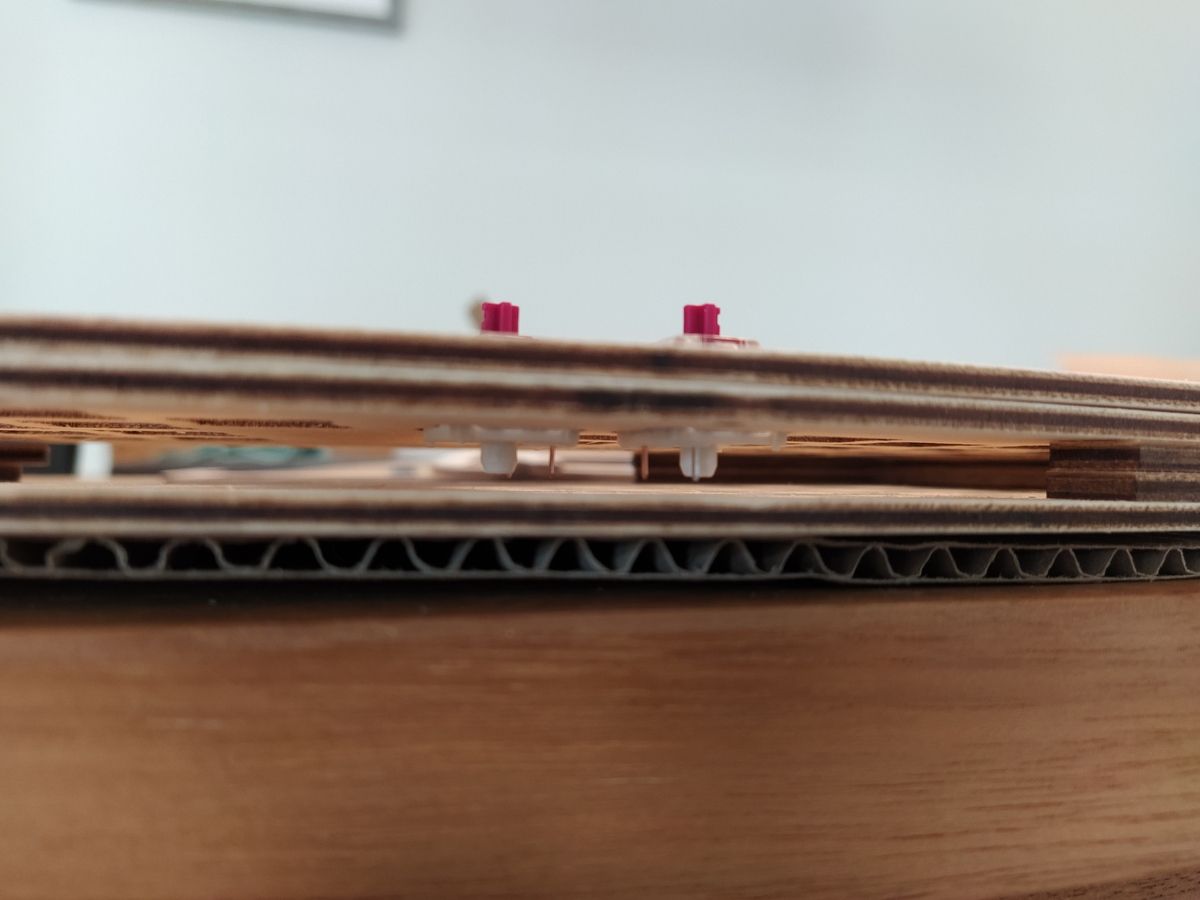 Side view of the sandwich assembly of the keyboard with five layers; two switches are positioned and their pins barely hover above the last layer.