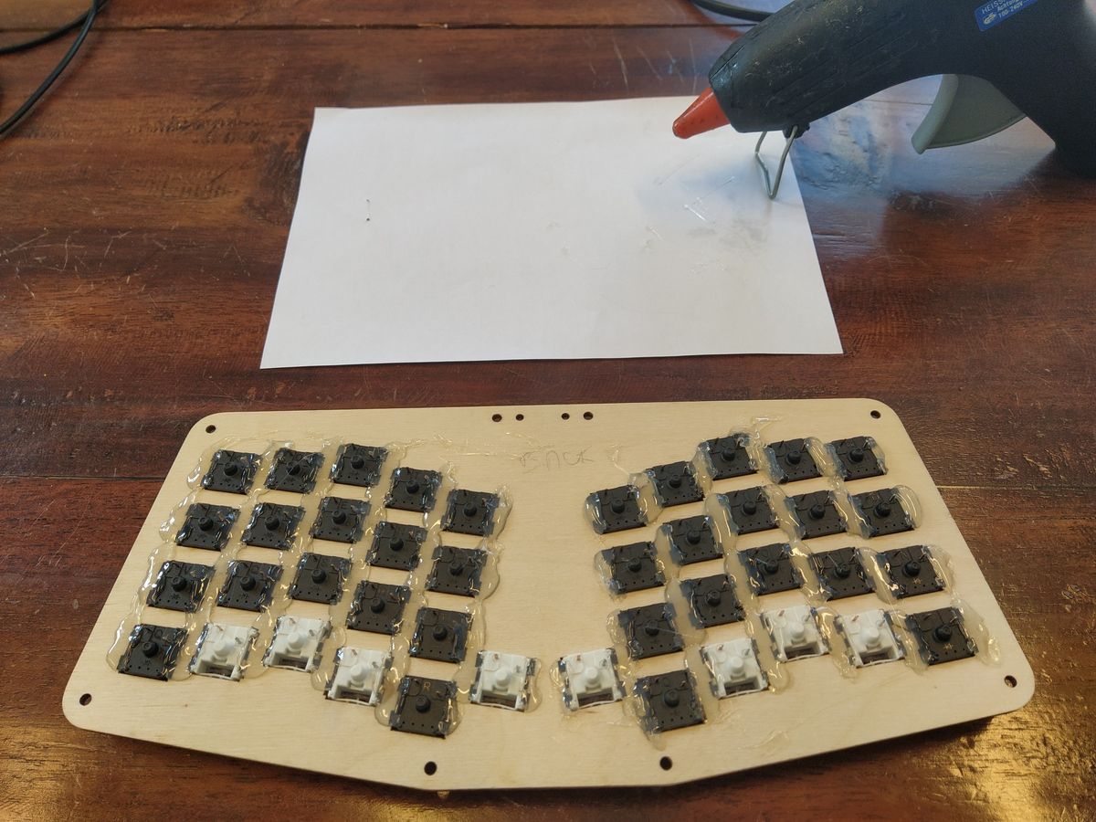 Keyboard base plate viewed from below with switches mounted on top. The switches have been (hot) glued to the wooden plate.